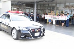 座喜味市長ら関係者が見送り、パトカーが先導し街頭パレードに出発した＝６日、市役所