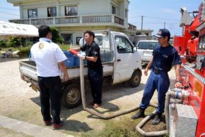 断水で給水車からポリタンクへ水を入れる地域住民（中央）＝２０１８年４月30日、伊良部国仲の伊良部中学校南側広場