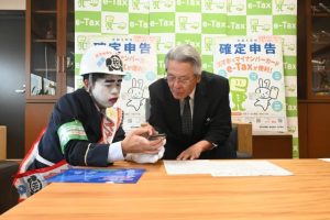 座喜味市長（右）が実際にスマホ申告を体験した＝29日、市役所