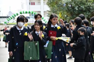 在校生や保護者が作るを花道を笑顔で歩く卒業生たち＝９日、平良中