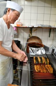 特製のタレをしみ込ませたウナギを丁寧に焼き上げる店主の下里さん＝２３日、平良西里「しきしま」