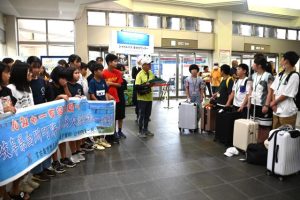 下地小の児童たち（左側）が横断幕で白川町からの交流団を出迎えた＝6日、宮古空港