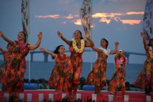 伊良部大橋と夕日を背にフラダンスを披露＝12日、トゥリバー海浜公園