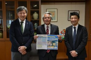 座喜味市長（中央）に初の大分県からのチャーター便就航を報告する伊藤執行役員（左）と長谷川支店長＝9日、市役所