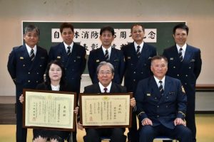 総理大臣表彰を受けた前川さん（前列中央）、日本防火・防災協会長表彰の下地代表（同左）。前列右は伝達した上地消防長＝19日、市消防本部